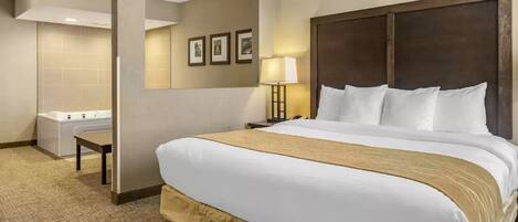 A hotel room with a large bed, a bedside table, a lamp, and a bathroom with a bathtub and sink.