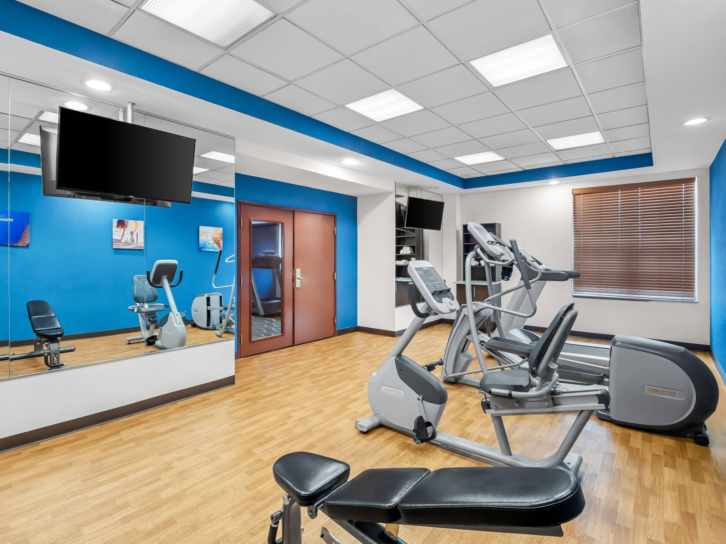 A gym with exercise equipment, a mirror, and a TV on the wall.
