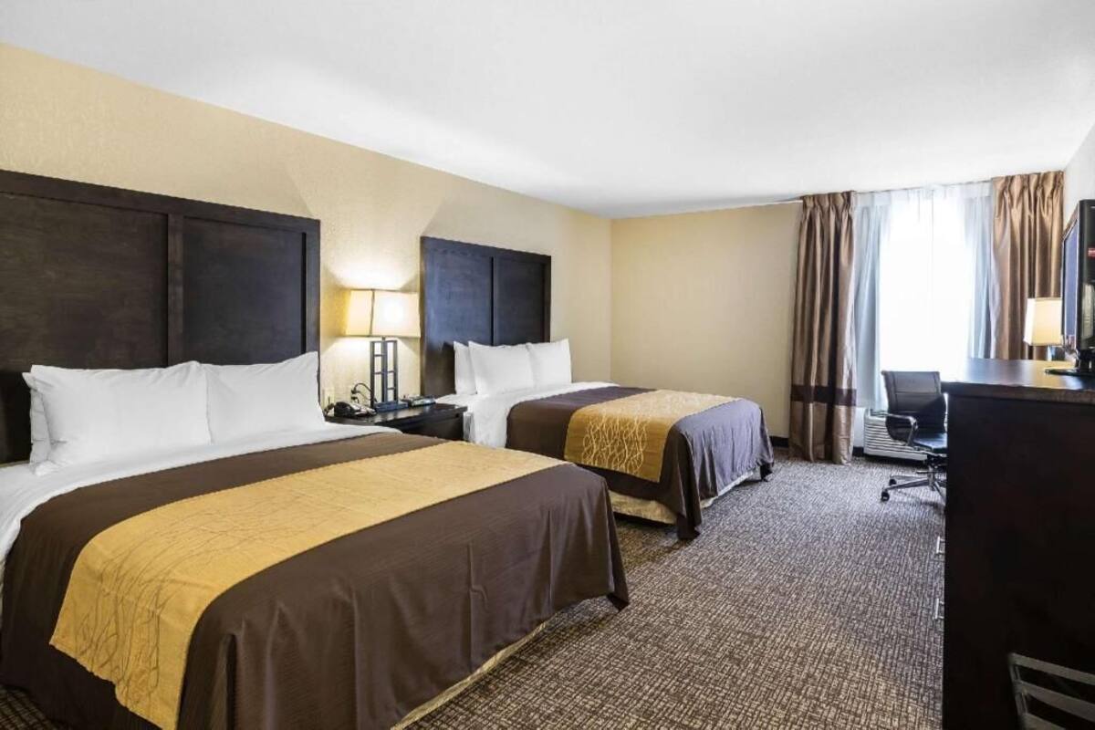 A hotel room with two beds, a desk, a chair, and a television.