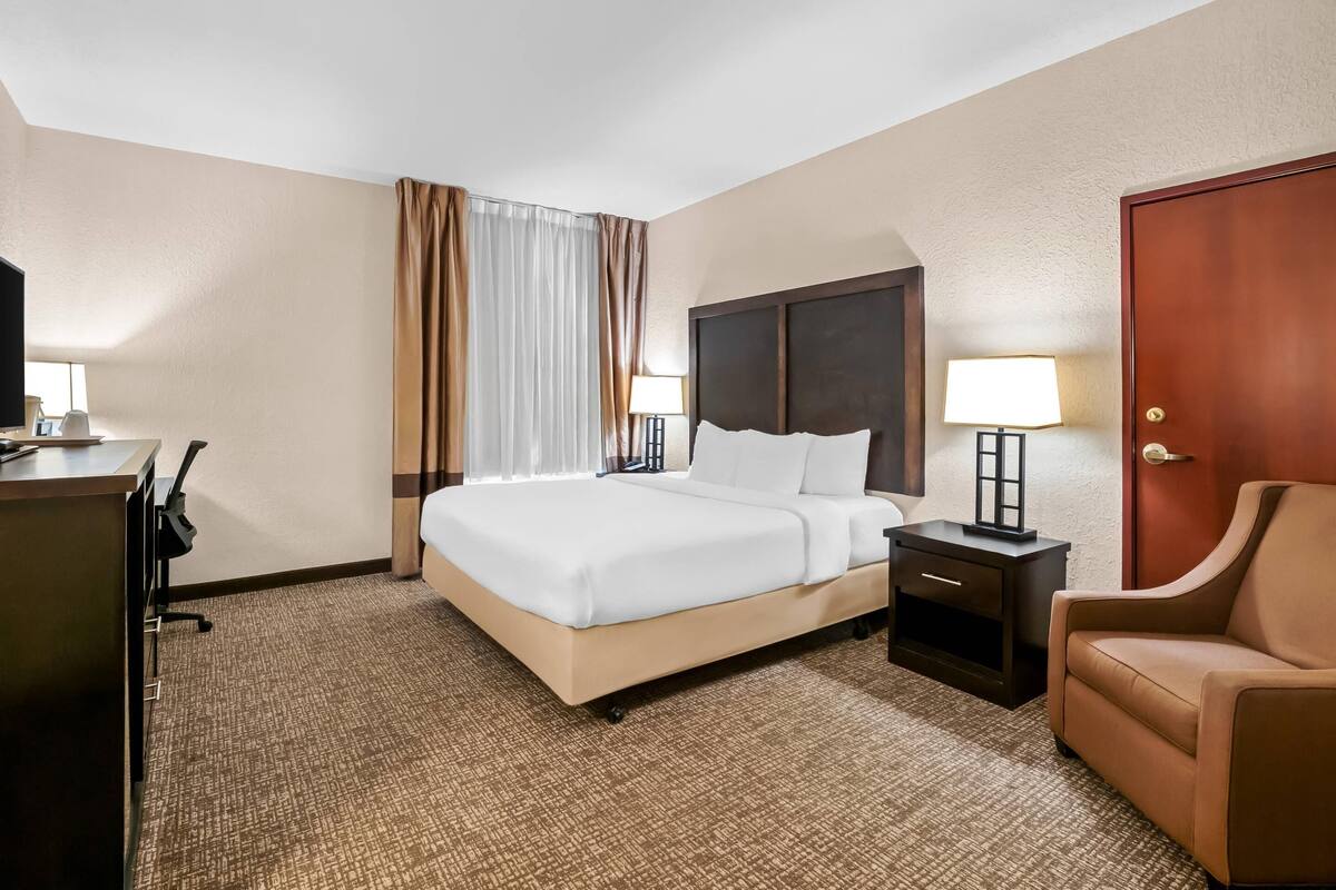 A hotel room with a bed, bedside tables, a desk, a chair, and a door.