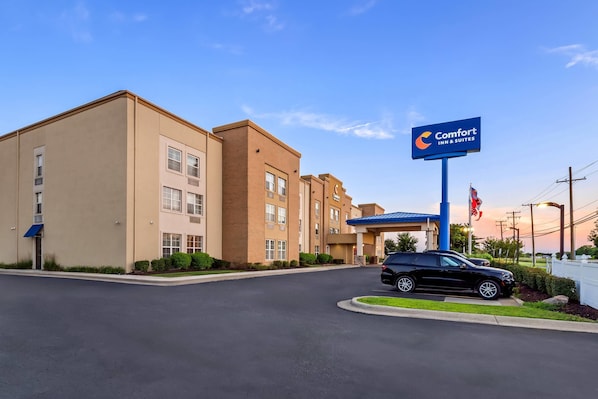 A Comfort Inn & Suites hotel with a blue sign, a parking lot, and a black SUV parked in front.