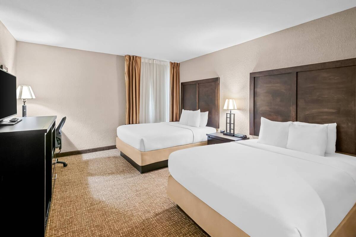 A hotel room with two beds, a desk, a TV, and a lamp.