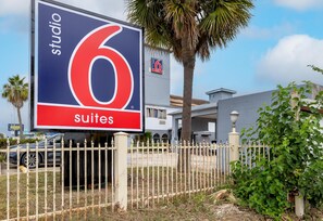A large sign for 'Studio 6 Suites' with a white fence and palm trees in the background. - Studio 6 Suites – Pasadena, TX (Pasadena)