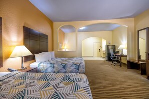 A hotel room with two beds, a desk, a chair, a TV, and a bathroom visible in the background. - Studio 6 Suites – Pasadena, TX (Pasadena)