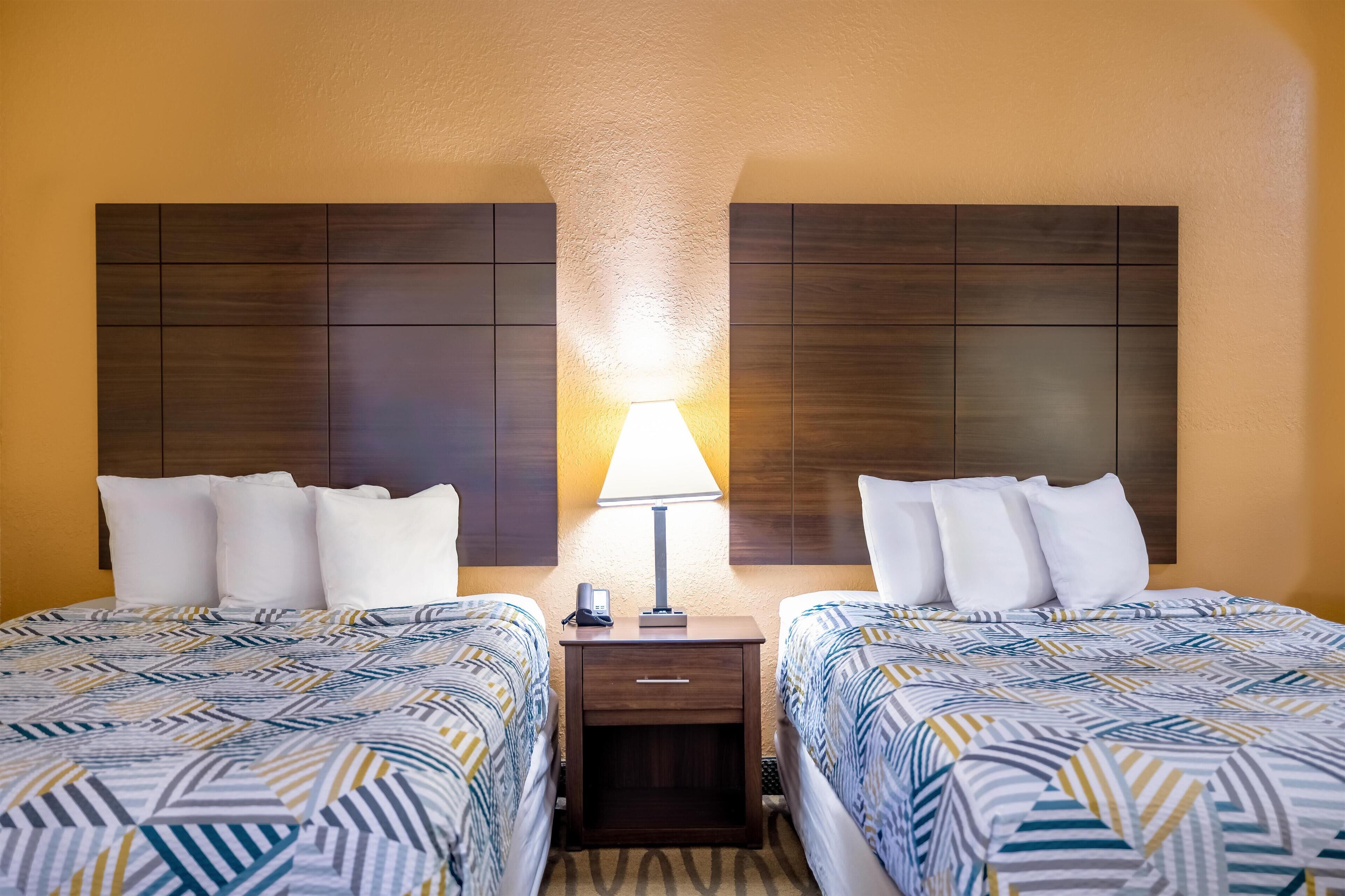A hotel room with two beds, a nightstand with a lamp, and a wooden headboard.