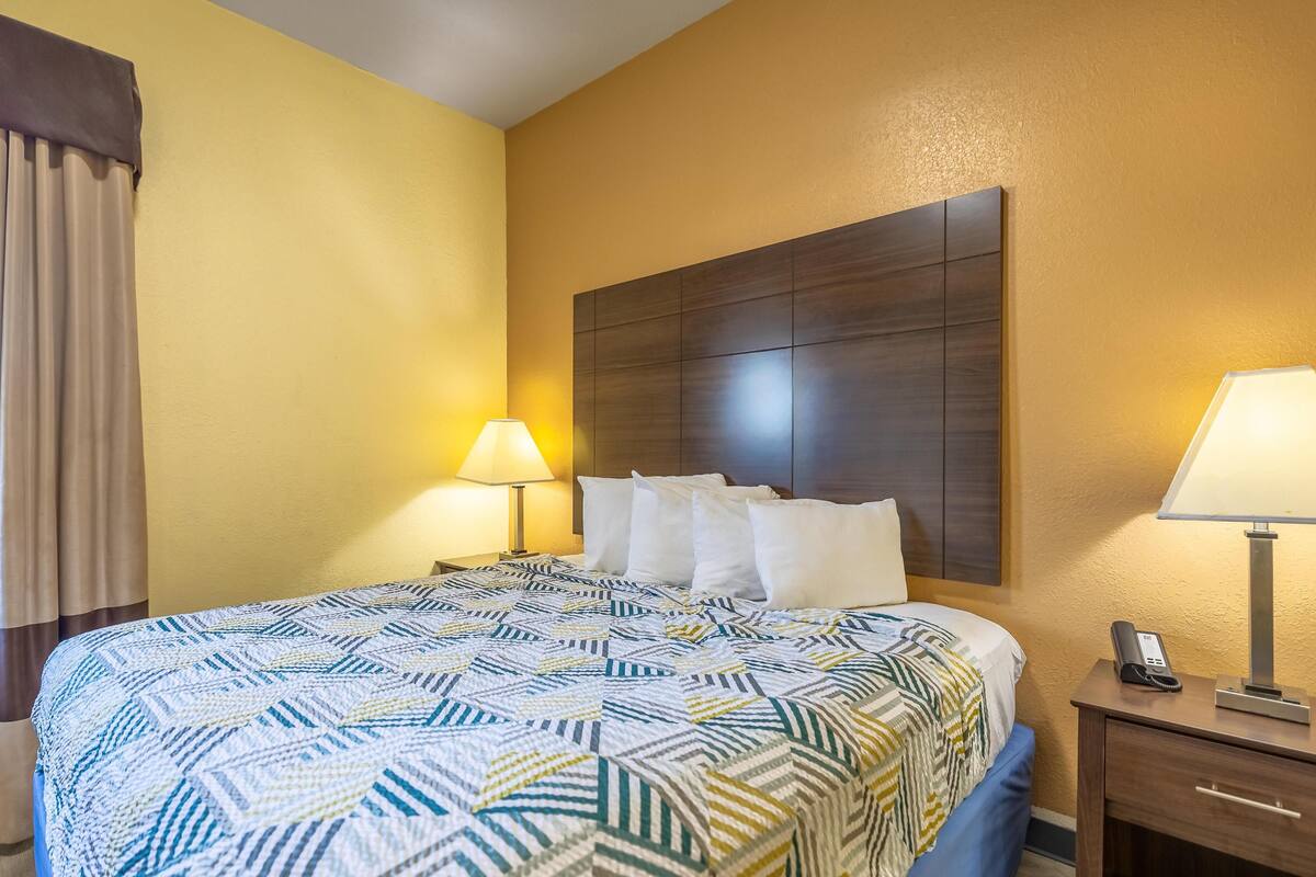 Une chambre d’hôtel avec un grand lit, deux lampes de chevet, une tête de lit en bois et un téléphone sur une table de chevet.