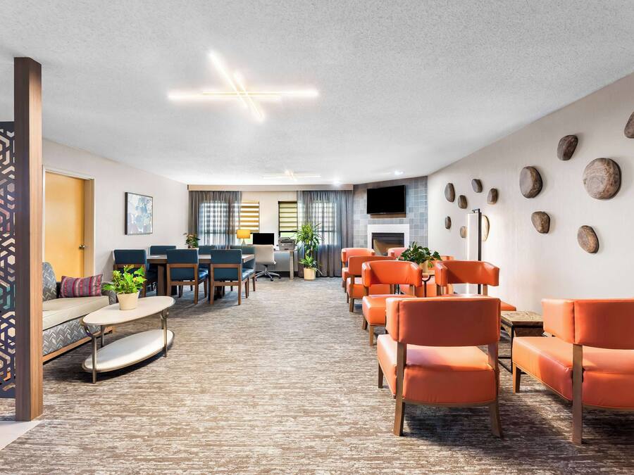 A modern living room with orange chairs, a sofa, and a coffee table. There is a TV mounted on the wall and a fireplace.