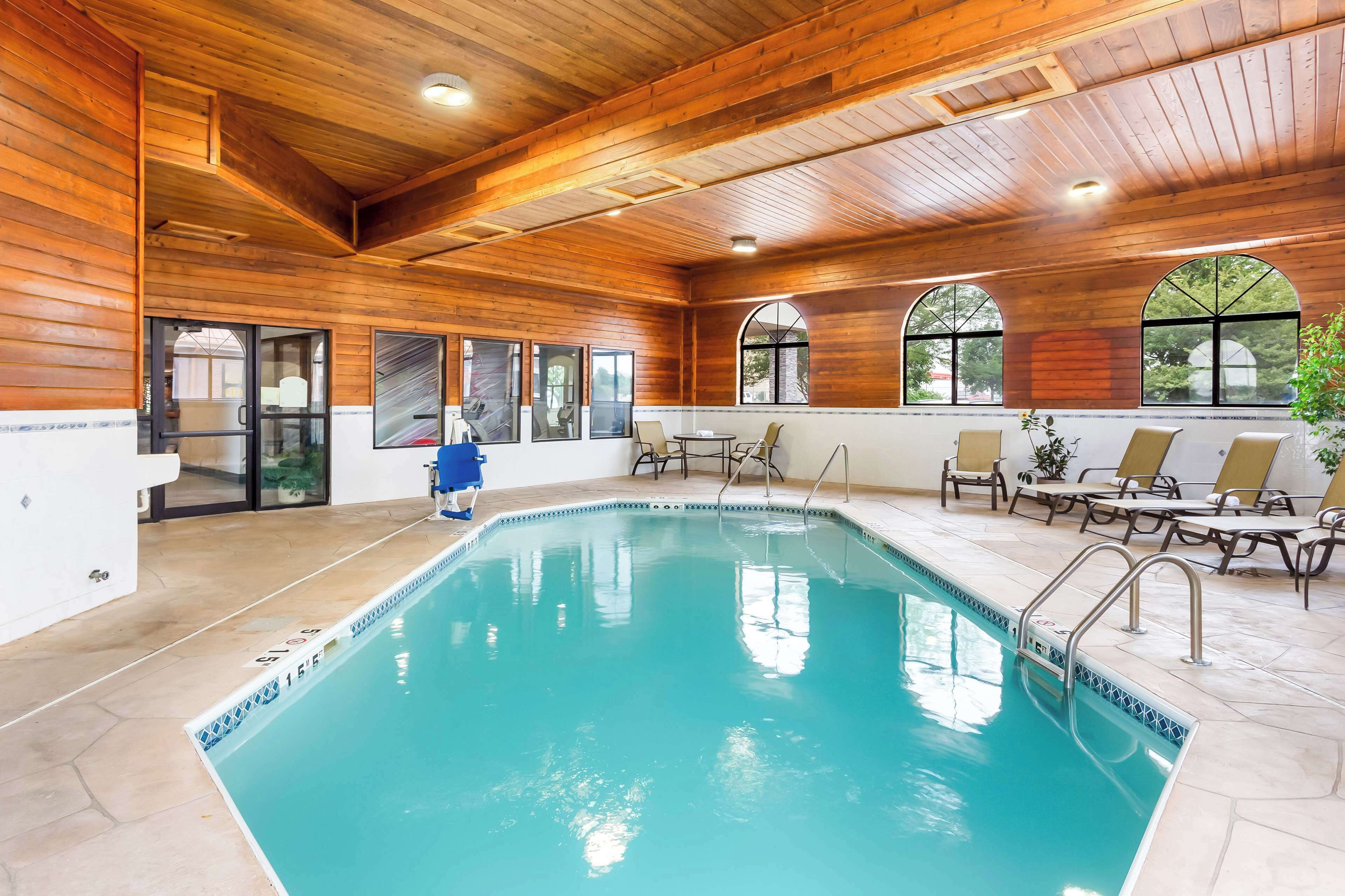 An indoor swimming pool with wooden walls and ceiling, clear glass doors, and lounge chairs around the pool area.