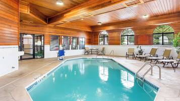 An indoor swimming pool with wooden walls and ceiling, clear glass doors, and lounge chairs around the pool area.