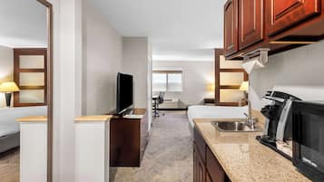 Una habitación de hotel pequeña con kitchenette, televisión, cama, escritorio y ventana.