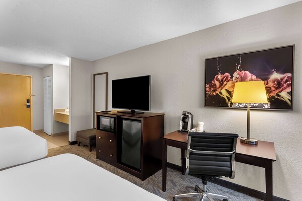 A hotel room with a bed, a desk with a chair, a television, a coffee maker, and a painting on the wall.
