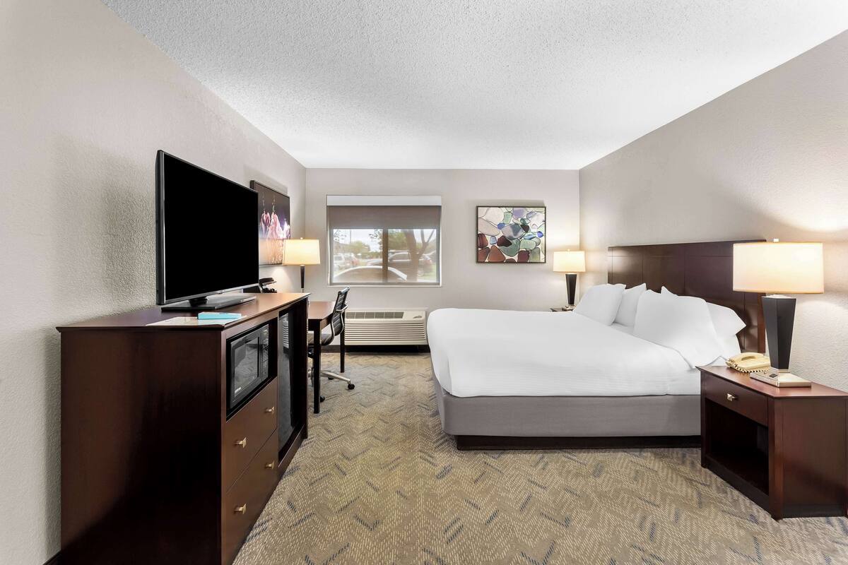 A hotel room with a bed, desk, television, and two bedside lamps.