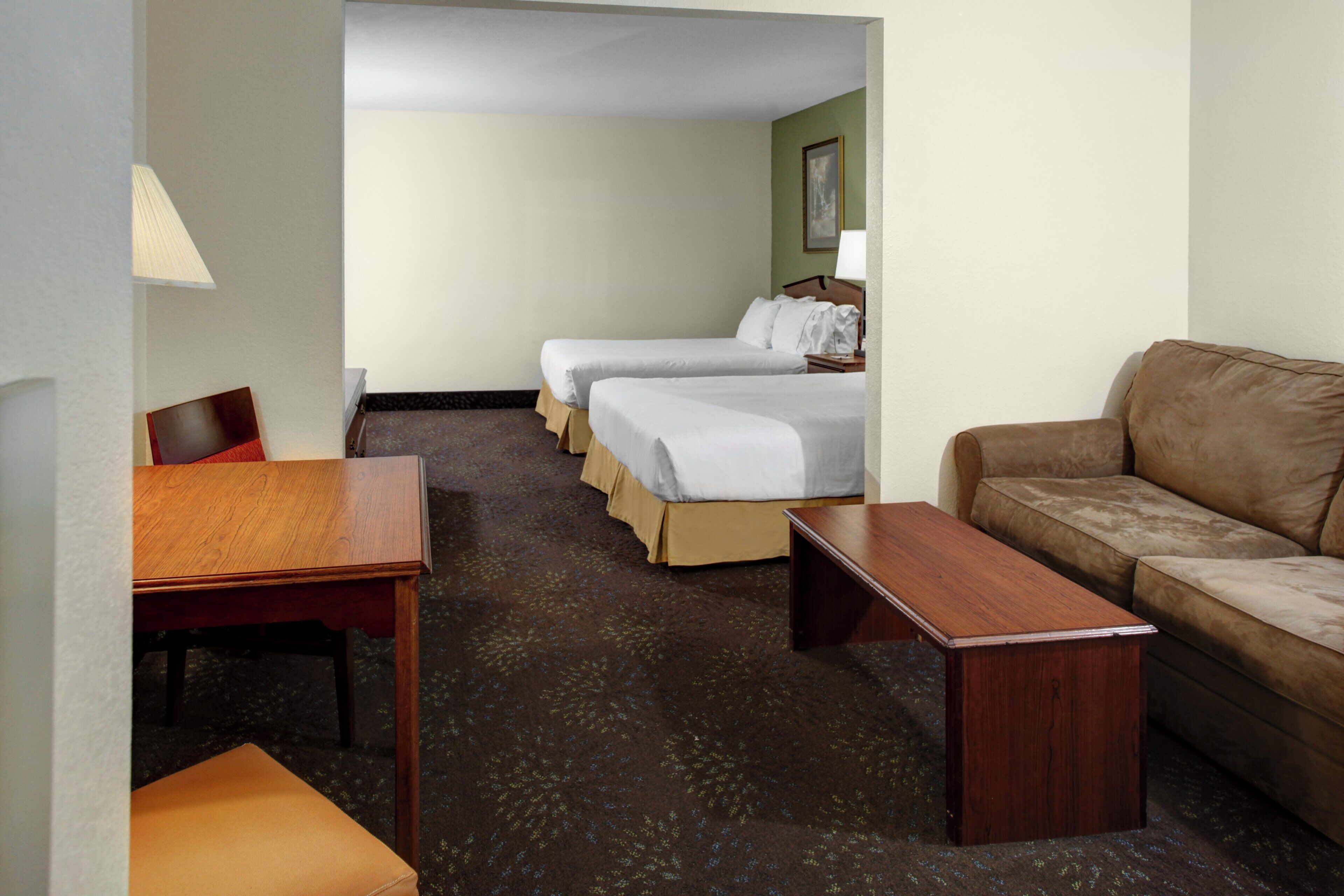 A hotel room with a wooden desk, two single beds, a sofa, and a carpeted floor.