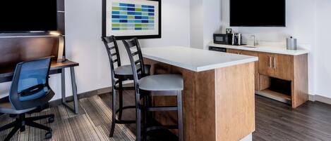 Una cocina moderna con una isla grande, taburetes de bar, una zona de comedor con mesa y sillas, y un televisor de pantalla plana montado sobre la isla.