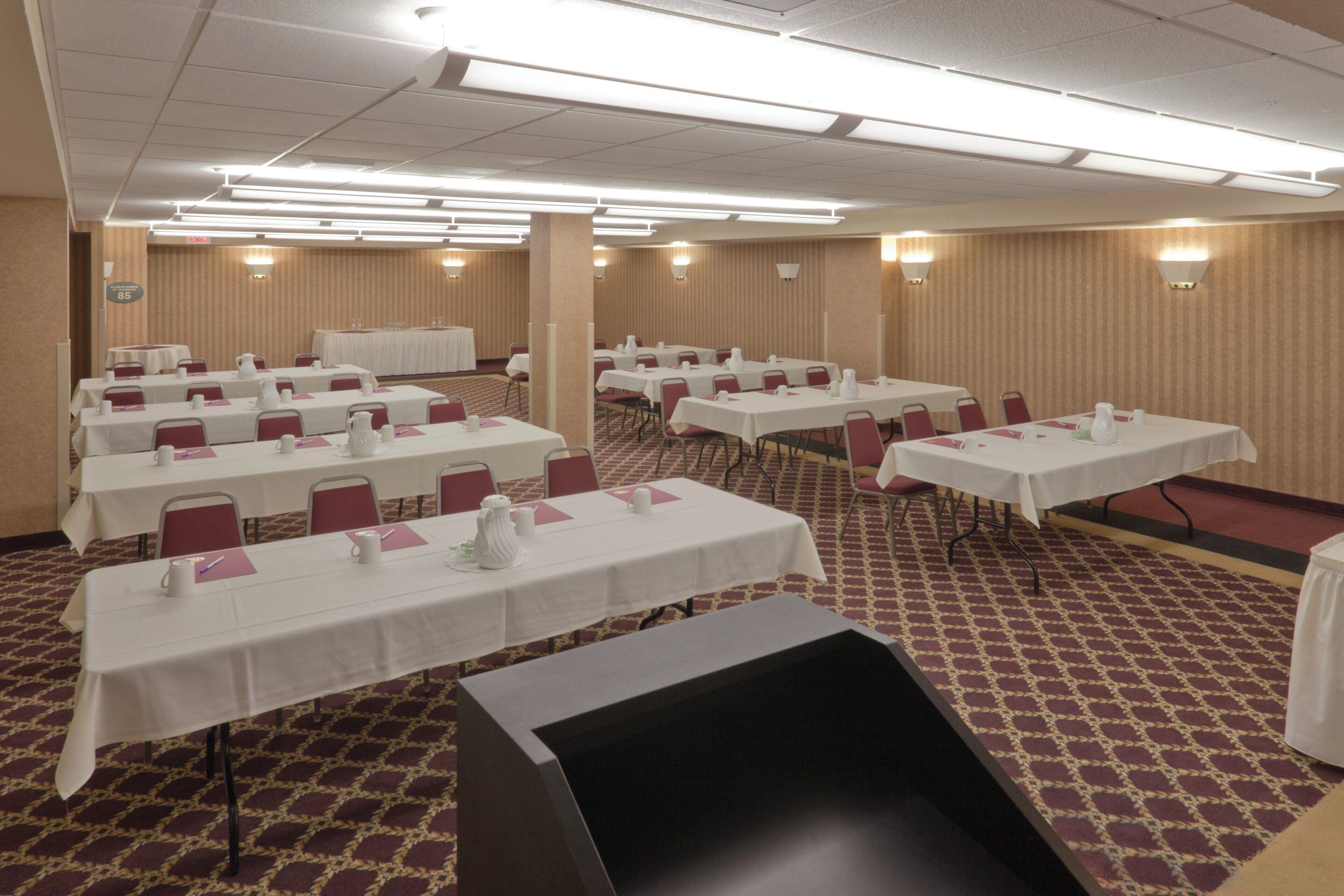 A conference room with multiple tables and chairs, arranged in rows.