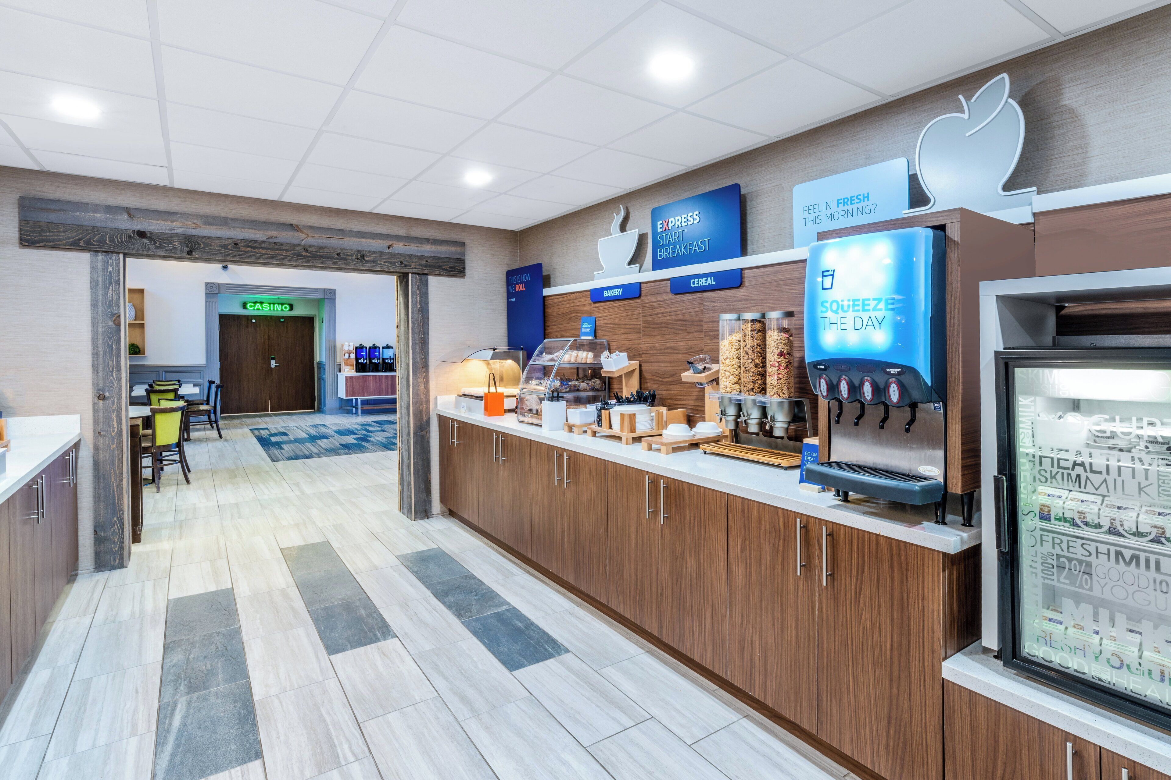 A modern breakfast area with a coffee machine, cereal dispenser, and a refrigerated display of milk and yogurt.