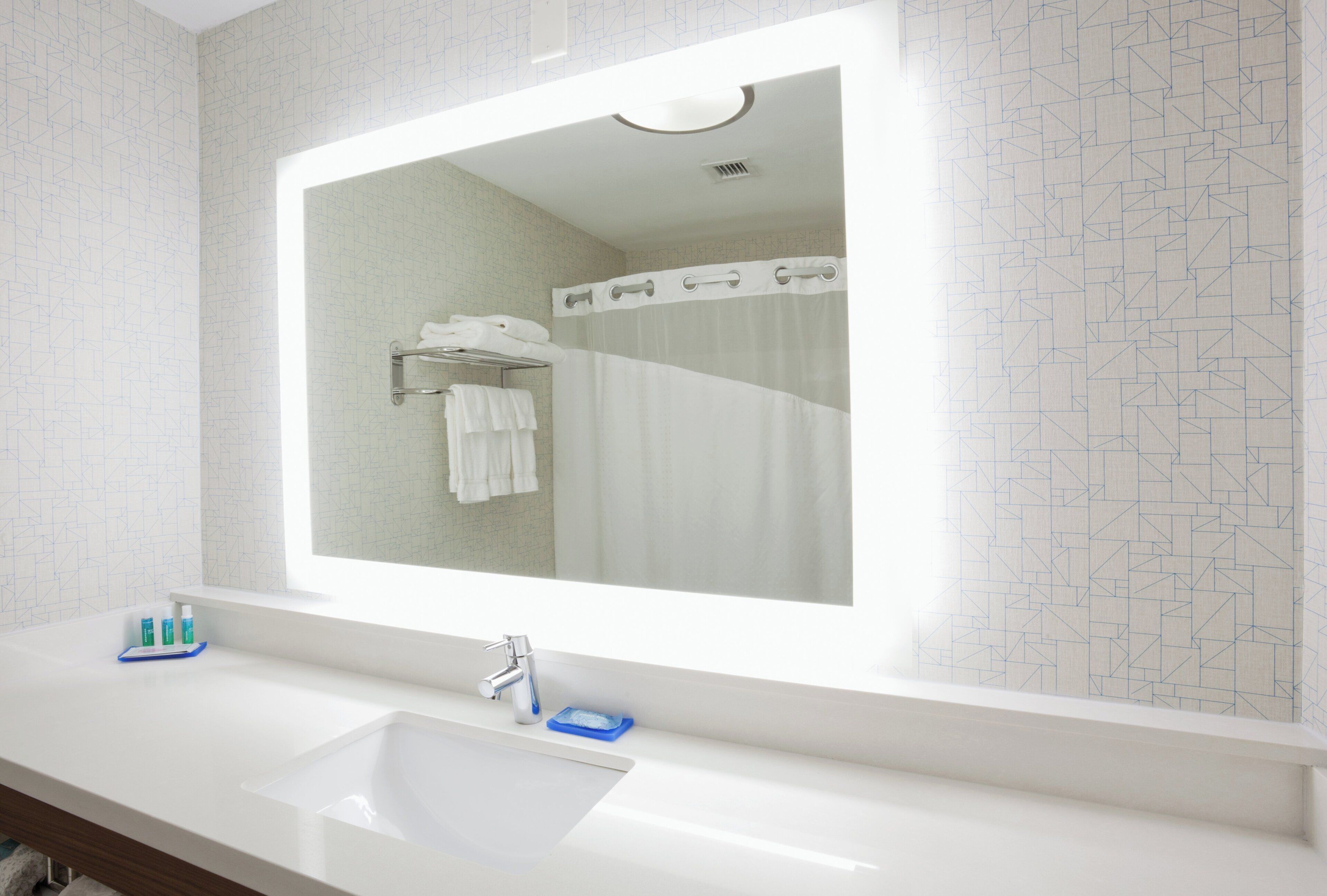 A bathroom with a large mirror, a sink, and a shower curtain.