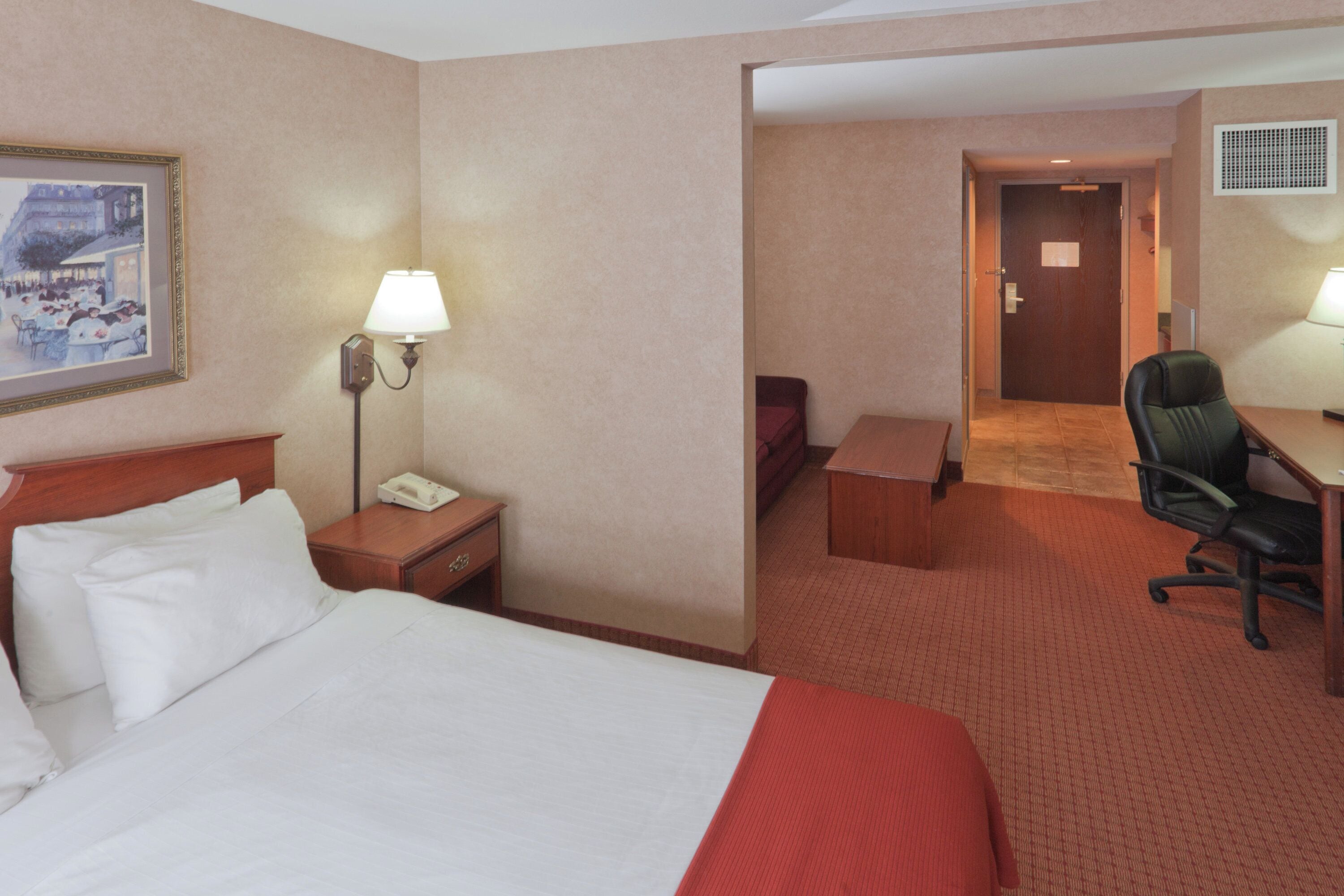 A hotel room with a bed, a desk, a chair, a telephone, and a lamp.