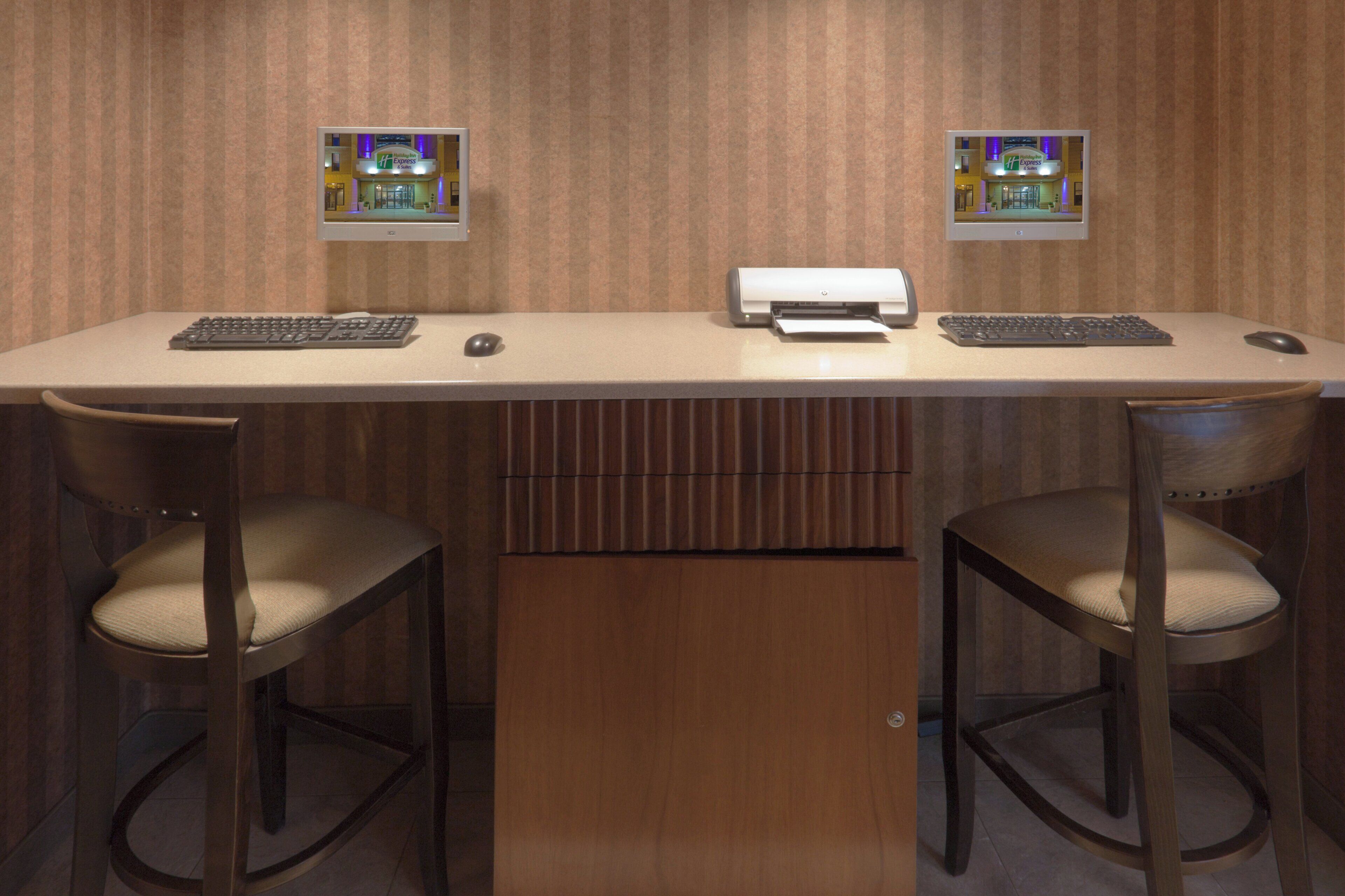 A hotel reception desk with two chairs, a printer, and two monitors displaying the hotel's name.
