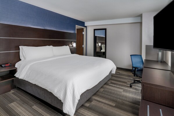 A hotel room with a large bed, a desk, a chair, a TV, and a mirror.