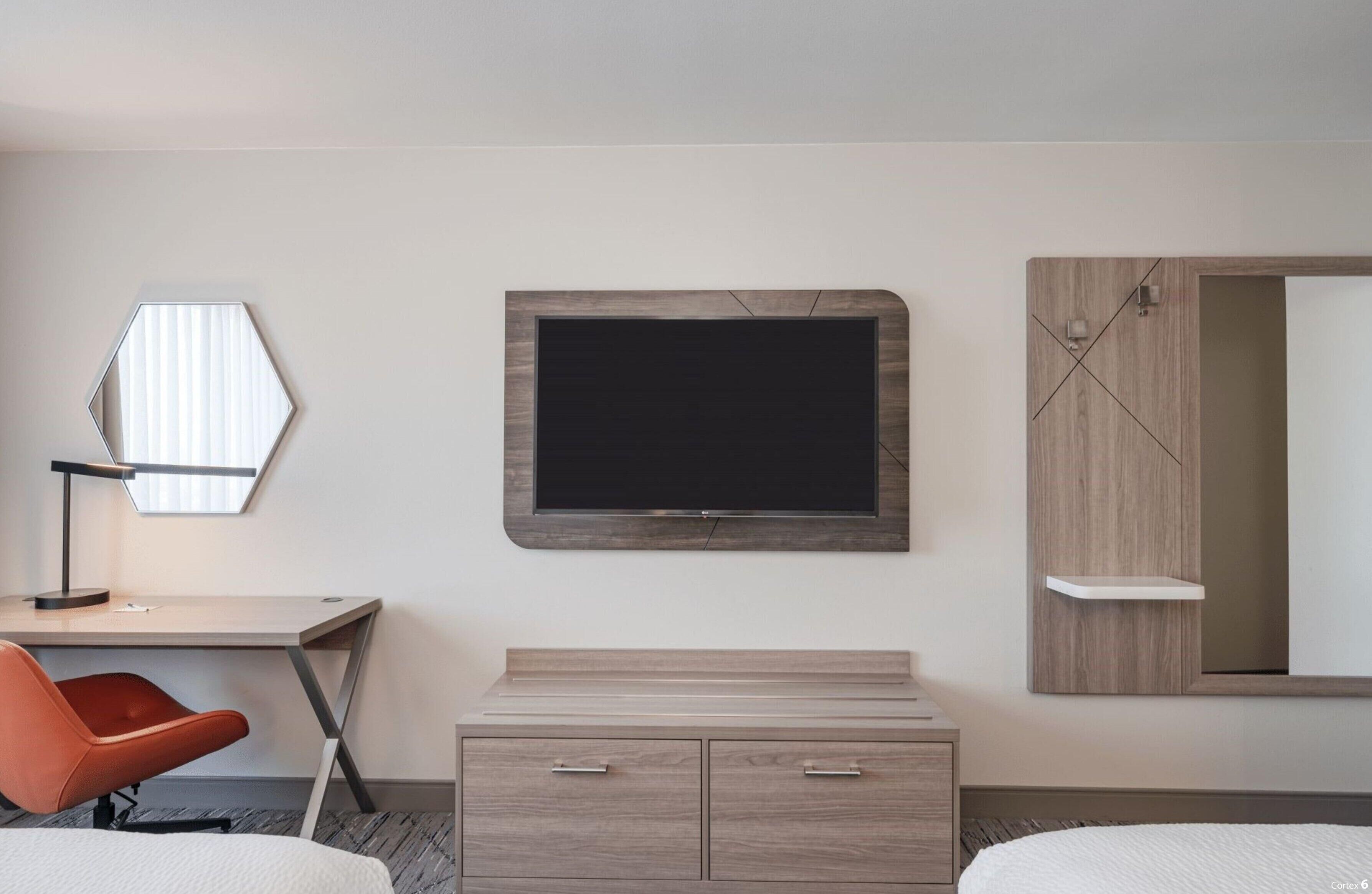 Una habitación de hotel con escritorio, televisor, espejo y cama.