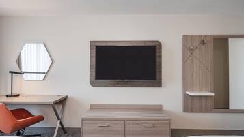 Una habitación de hotel con escritorio, televisor, espejo y cama.