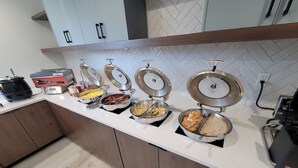 A buffet setup with various food items in metal containers, a coffee machine, and a rice cooker on a kitchen counter. - Holiday Inn Express Federal Way Seattle South by IHG (Federal Way)