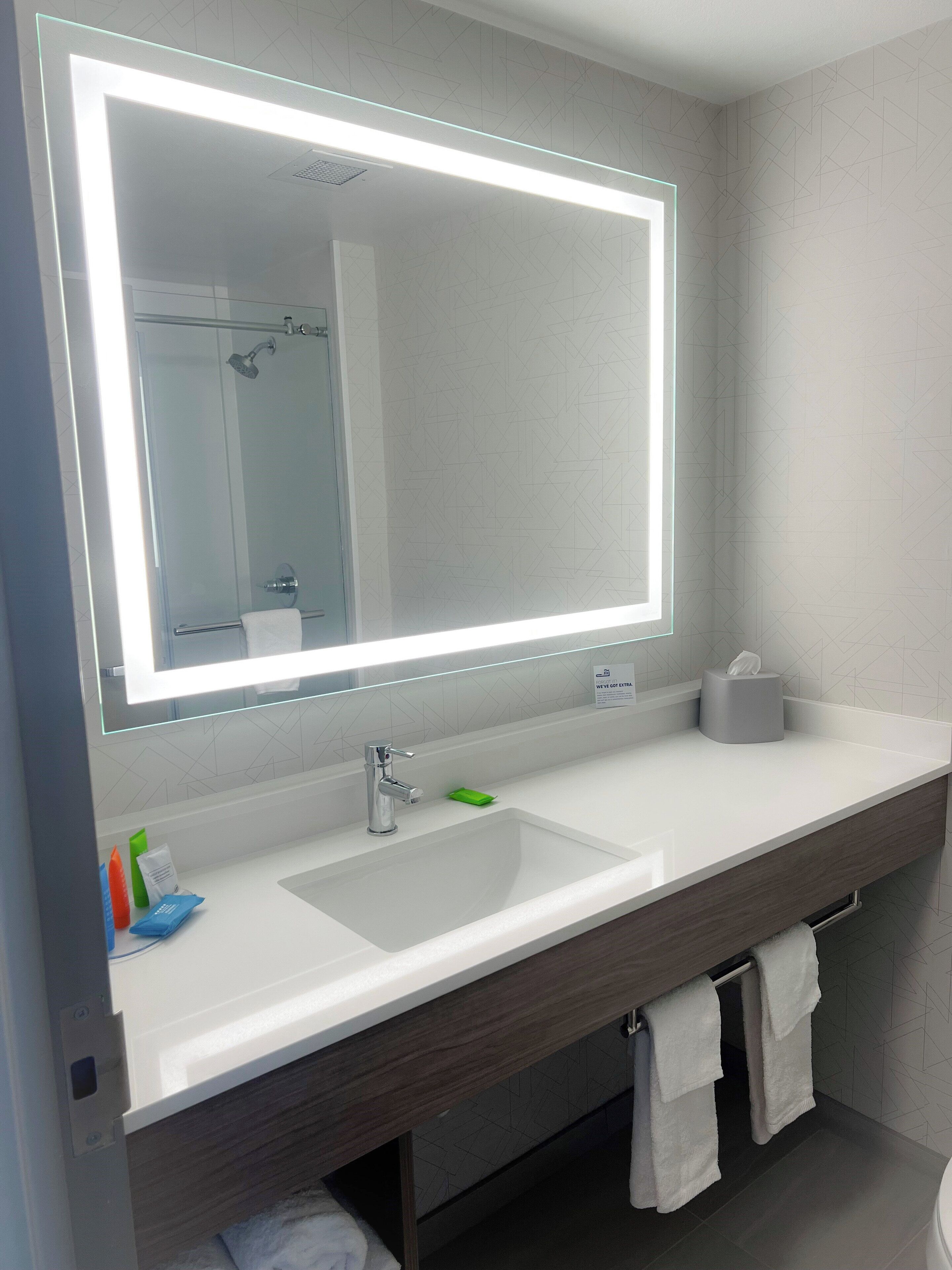 A modern bathroom with a large mirror, white sink, and a towel rack.