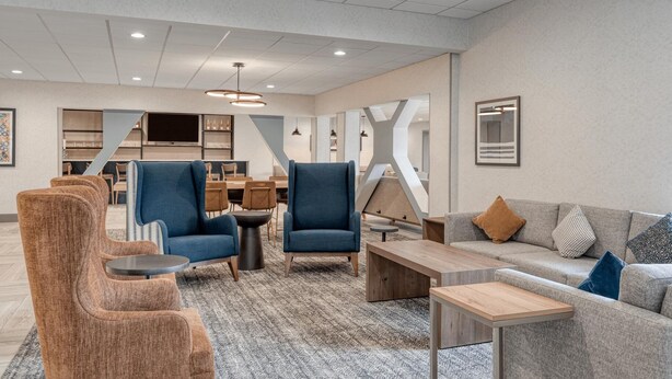 A spacious lobby with a modern design, featuring a seating area with sofas and armchairs, a wooden coffee table, and a dining area with a long table and chairs. - Holiday Inn Express Federal Way Seattle South by IHG (Federal Way)