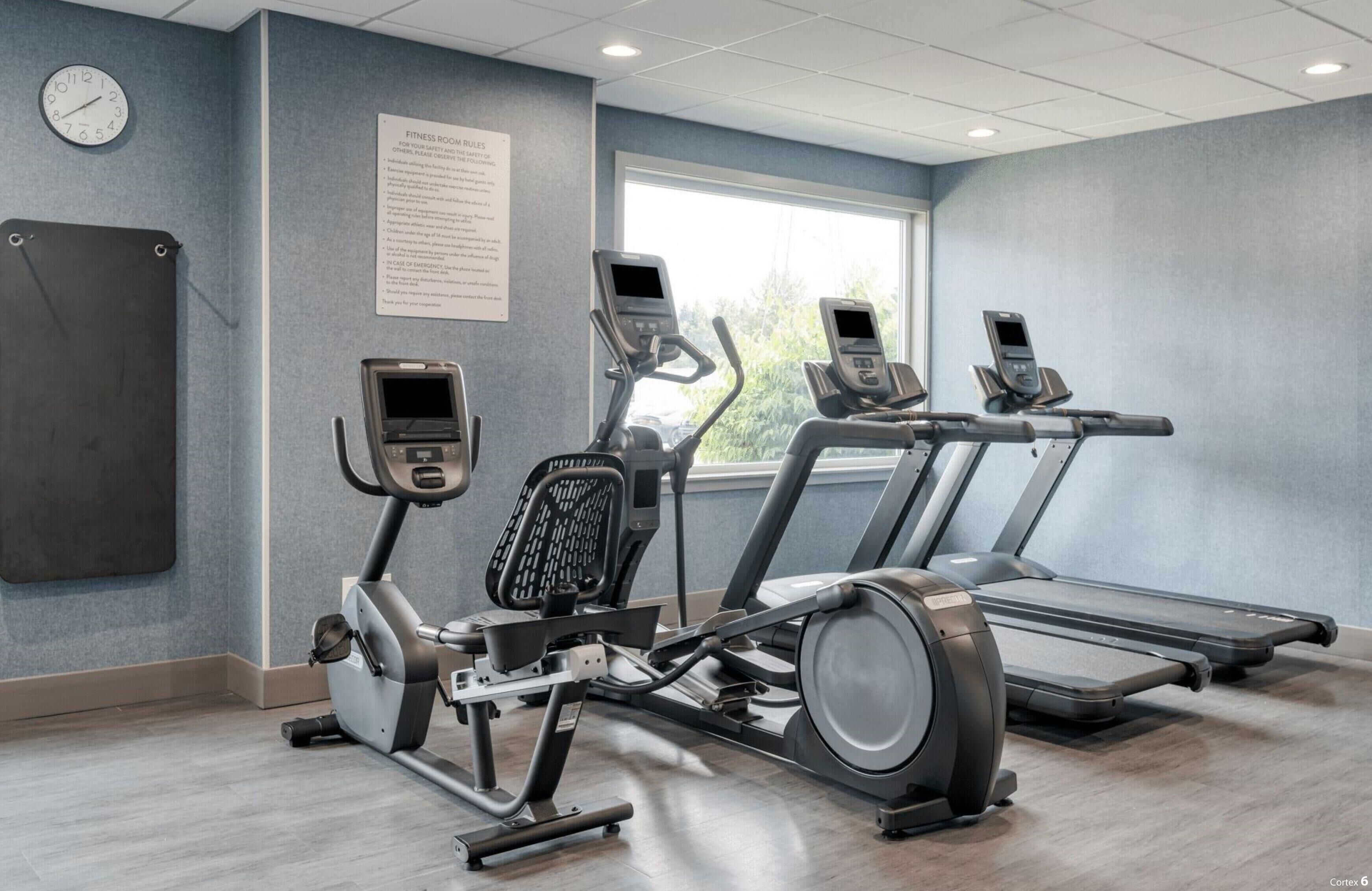 Une salle de sport équipée de tapis de course, d’un vélo elliptique et d’une horloge murale.