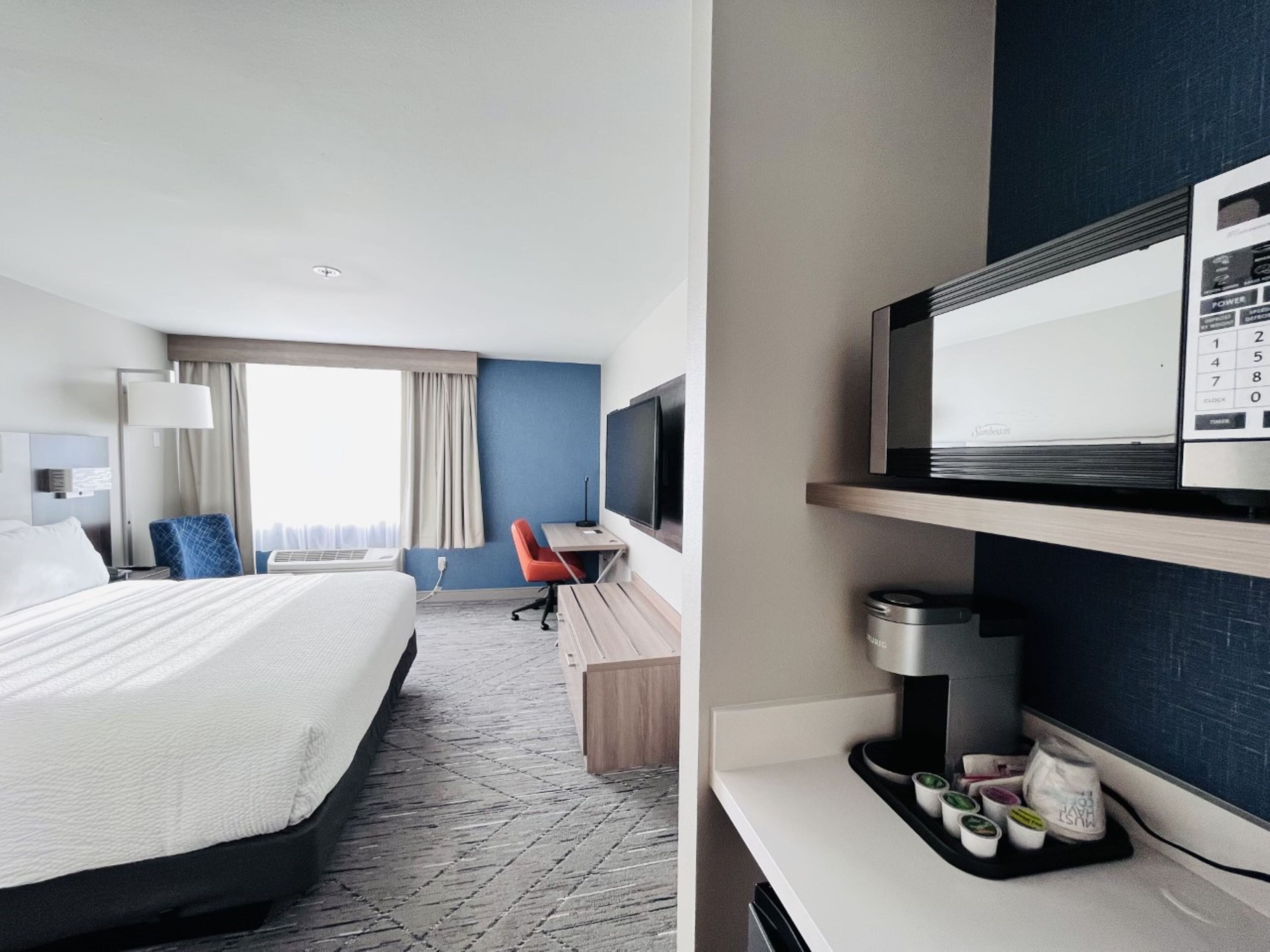 Ein Hotelzimmer mit Bett, Schreibtisch, Stuhl, Fernseher und einem Tablett mit Speisen.