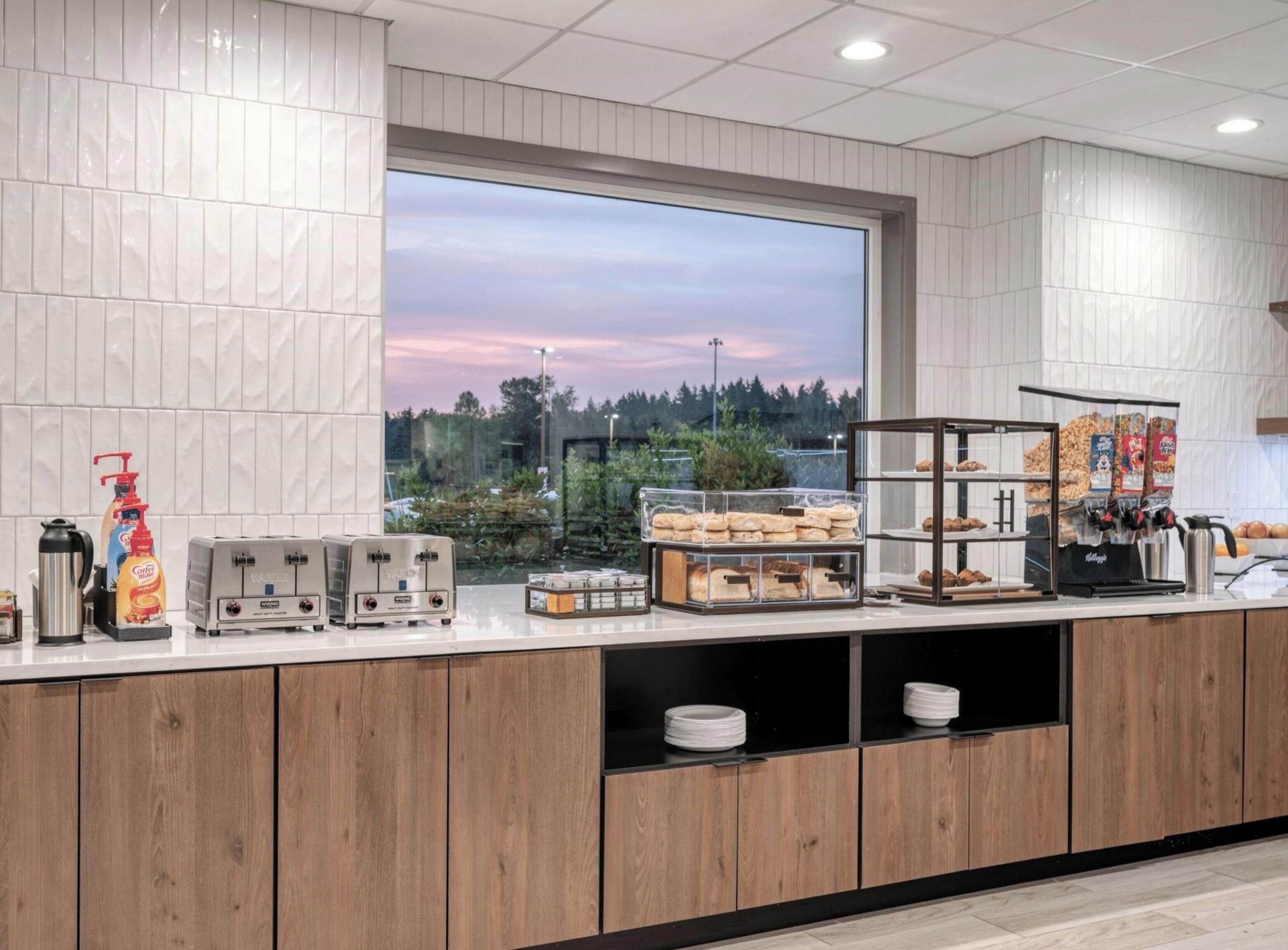 A modern kitchen with a large window, wooden cabinets, and various food items and appliances.