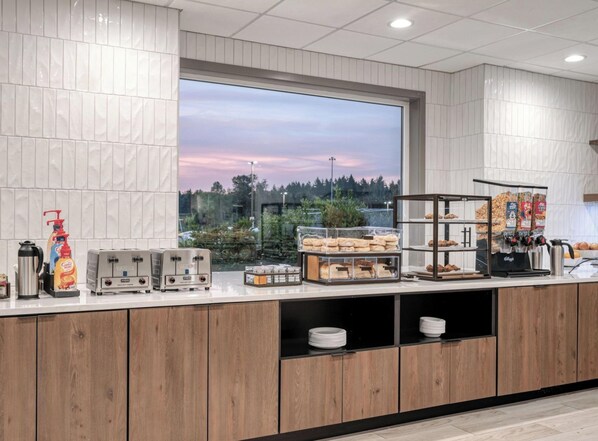 A modern kitchen with a large window, wooden cabinets, and various food items and appliances. - Holiday Inn Express Federal Way Seattle South by IHG (Federal Way)