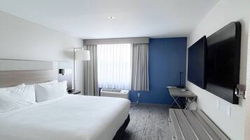 A modern hotel room with a large bed, a desk, a flat-screen TV, and a window with curtains.