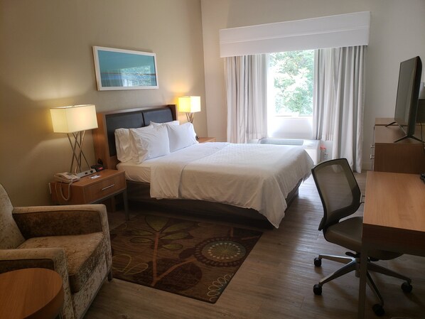 A hotel room with a bed, bedside lamps, a desk, a chair, a television, and a window with curtains.