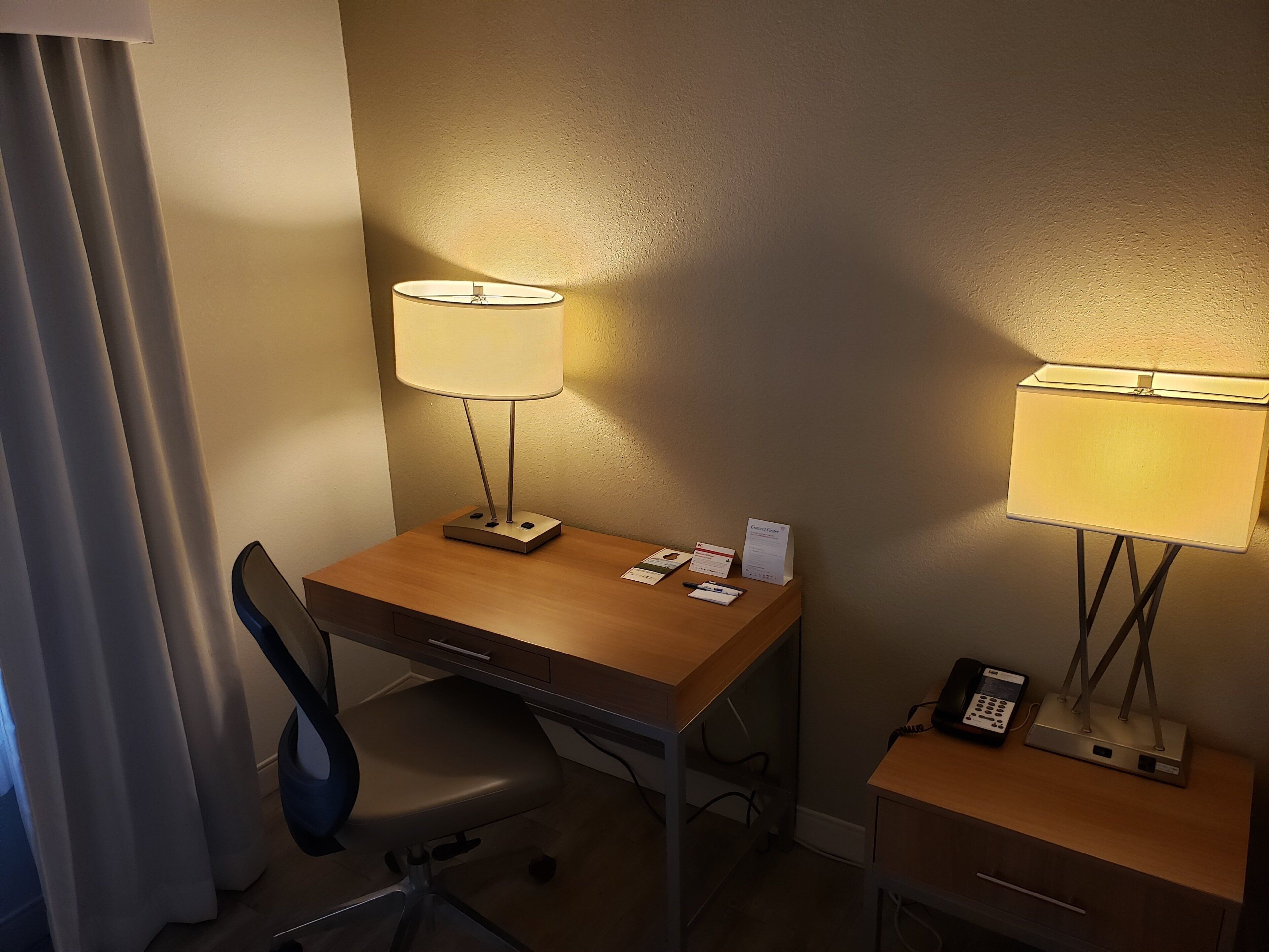 Une chambre d’hôtel équipée d’un bureau, d’une chaise, d’une lampe, d’un téléphone et d’un petit placard.