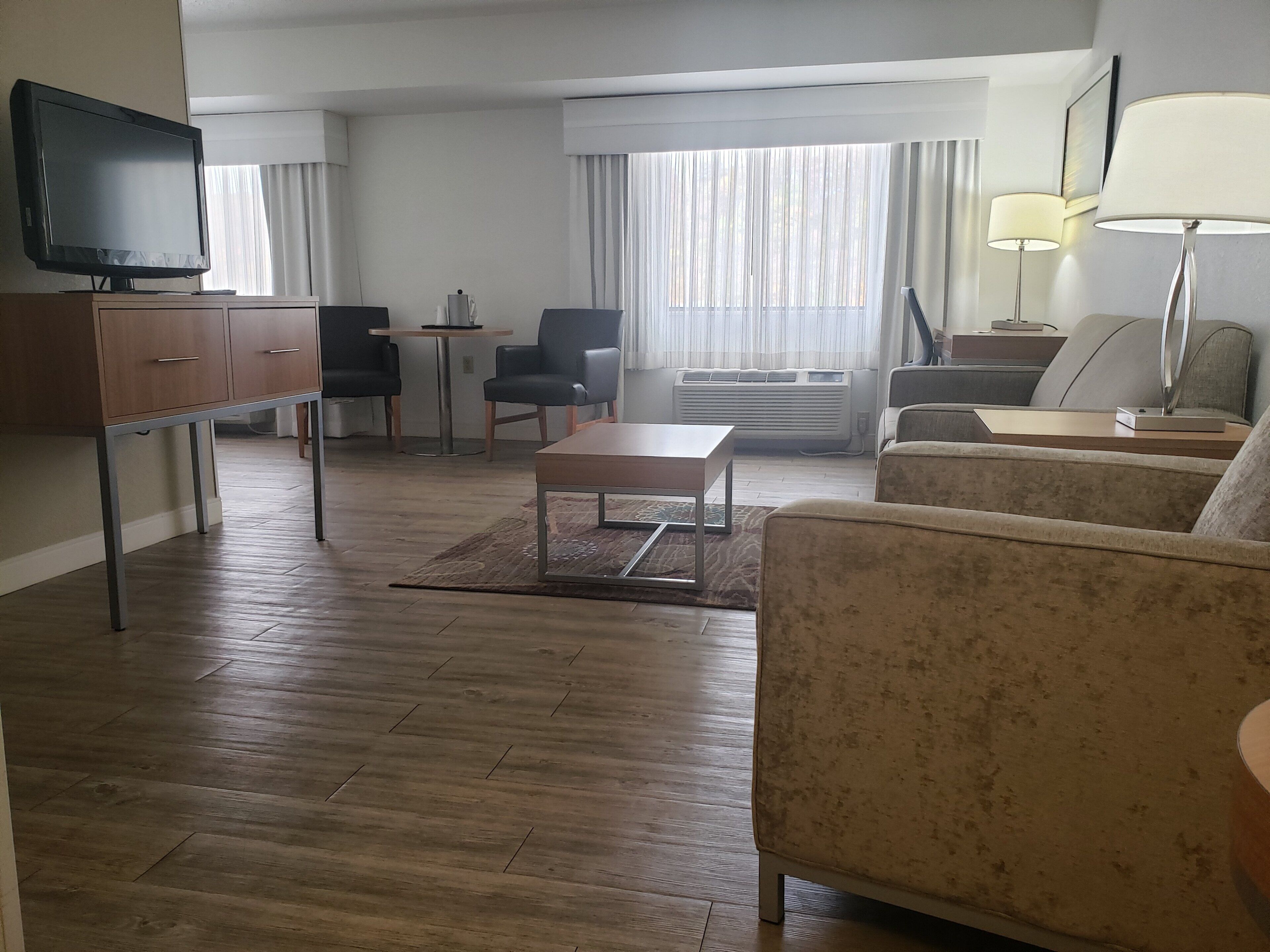 A hotel room with a flat-screen TV, a sofa, a coffee table, a desk, and a chair.