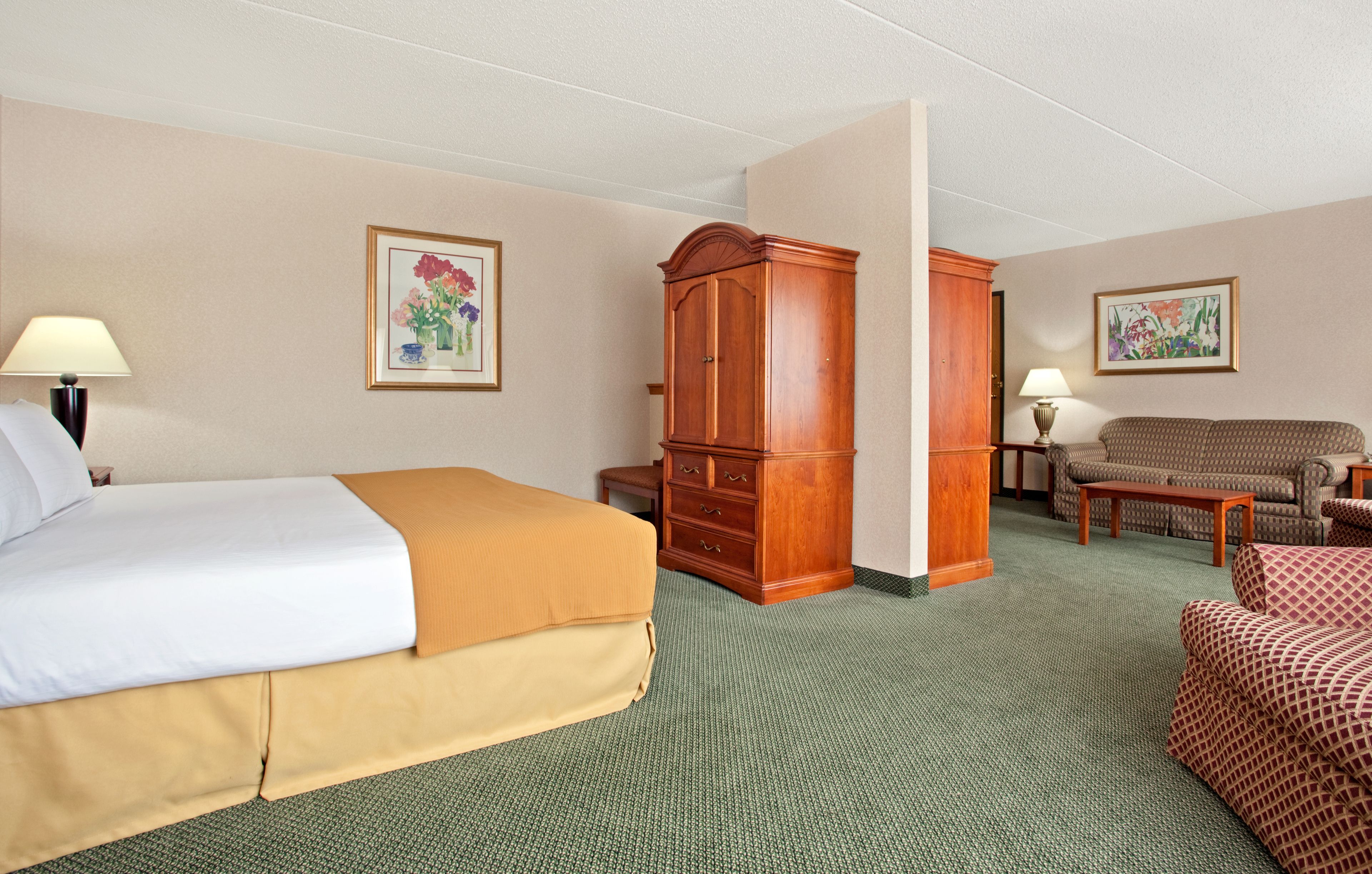 A hotel room with a bed, a wooden wardrobe, a sofa, and two lamps.