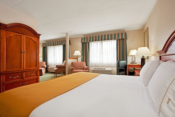 Een hotelkamer met een groot bed, een houten garderobe, een bureau met stoel, een klein tafeltje en twee lampen.