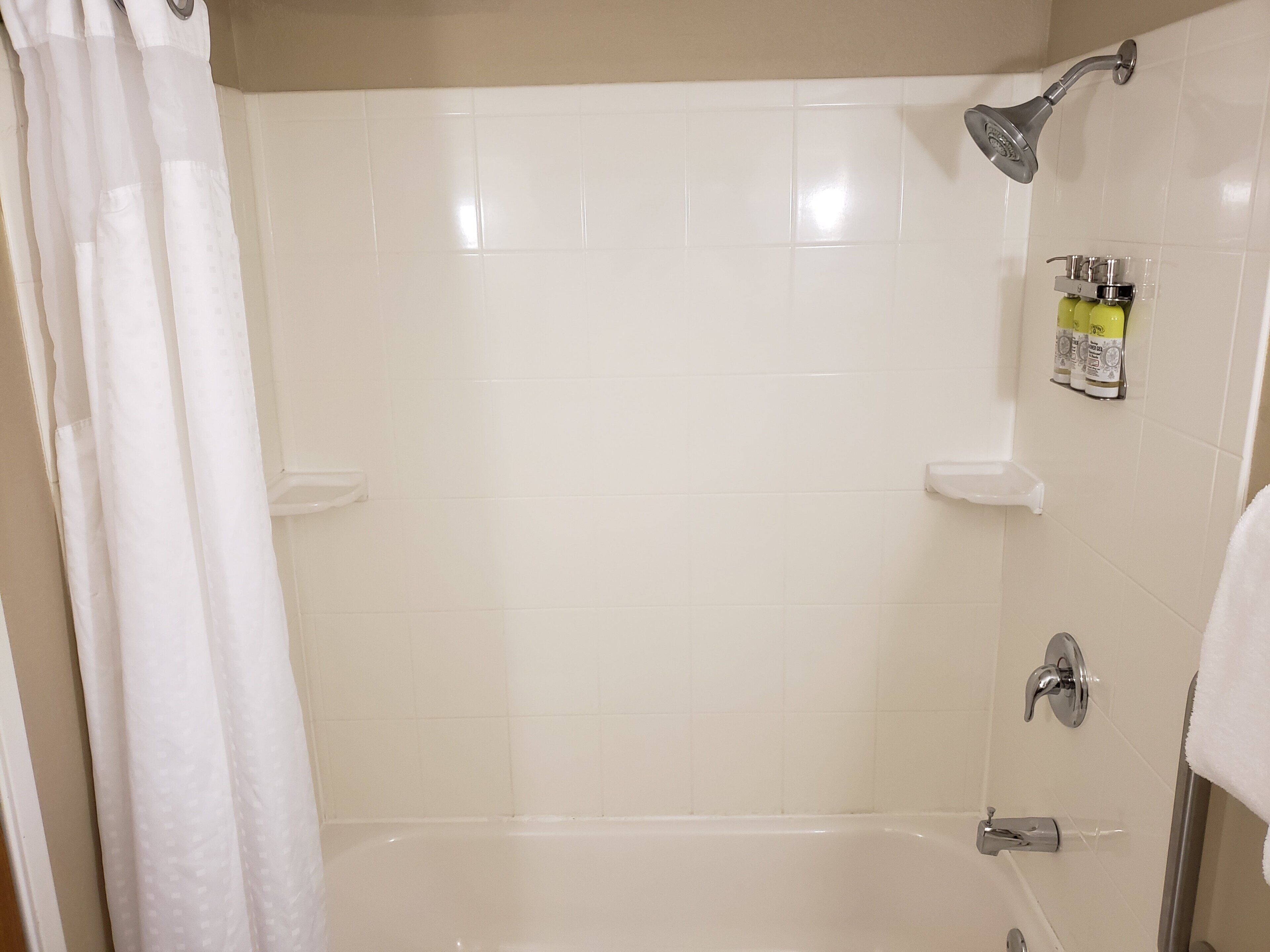 Et badeværelse med badekar, brusehoved, håndklædestang og sæbedispenser.