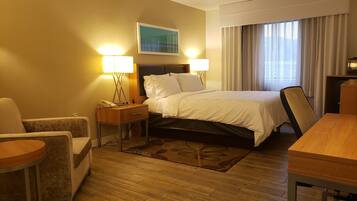 Une chambre d’hôtel avec un lit, deux lampes de chevet, un bureau, une chaise, une table de chevet et un tableau au mur.