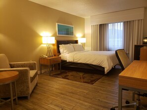 A hotel room with a bed, two bedside lamps, a desk, a chair, a nightstand, and a painting on the wall.