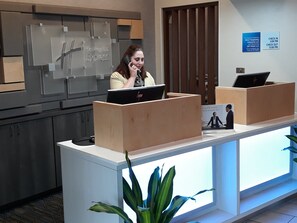 A reception desk with a computer, a sign for Holiday Inn Express, and a check-in/out schedule.