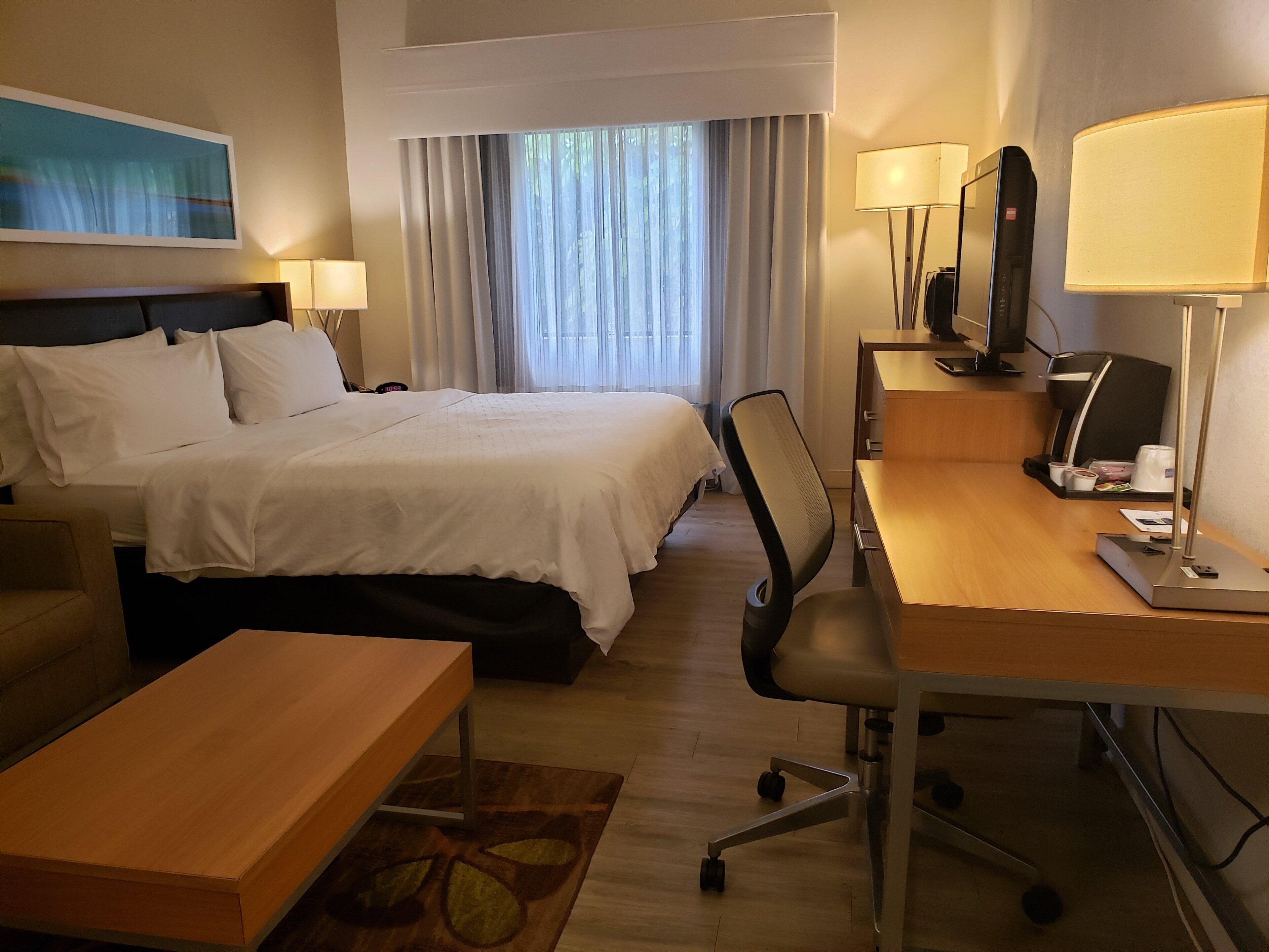 A hotel room with a bed, a desk, a chair, a coffee machine, and a television.
