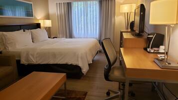 A hotel room with a bed, a desk, a chair, a coffee machine, and a television.