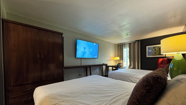 A hotel room with two beds, a TV, a desk, and a lamp. - Lux Hotel (Cordele)