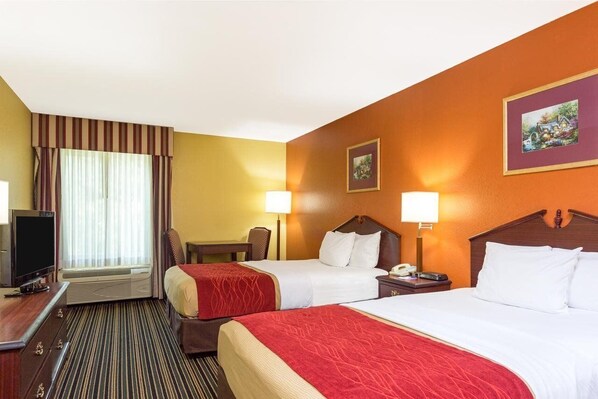 A hotel room with two beds, a TV, a desk, and a window with curtains. - Lux Hotel (Cordele)