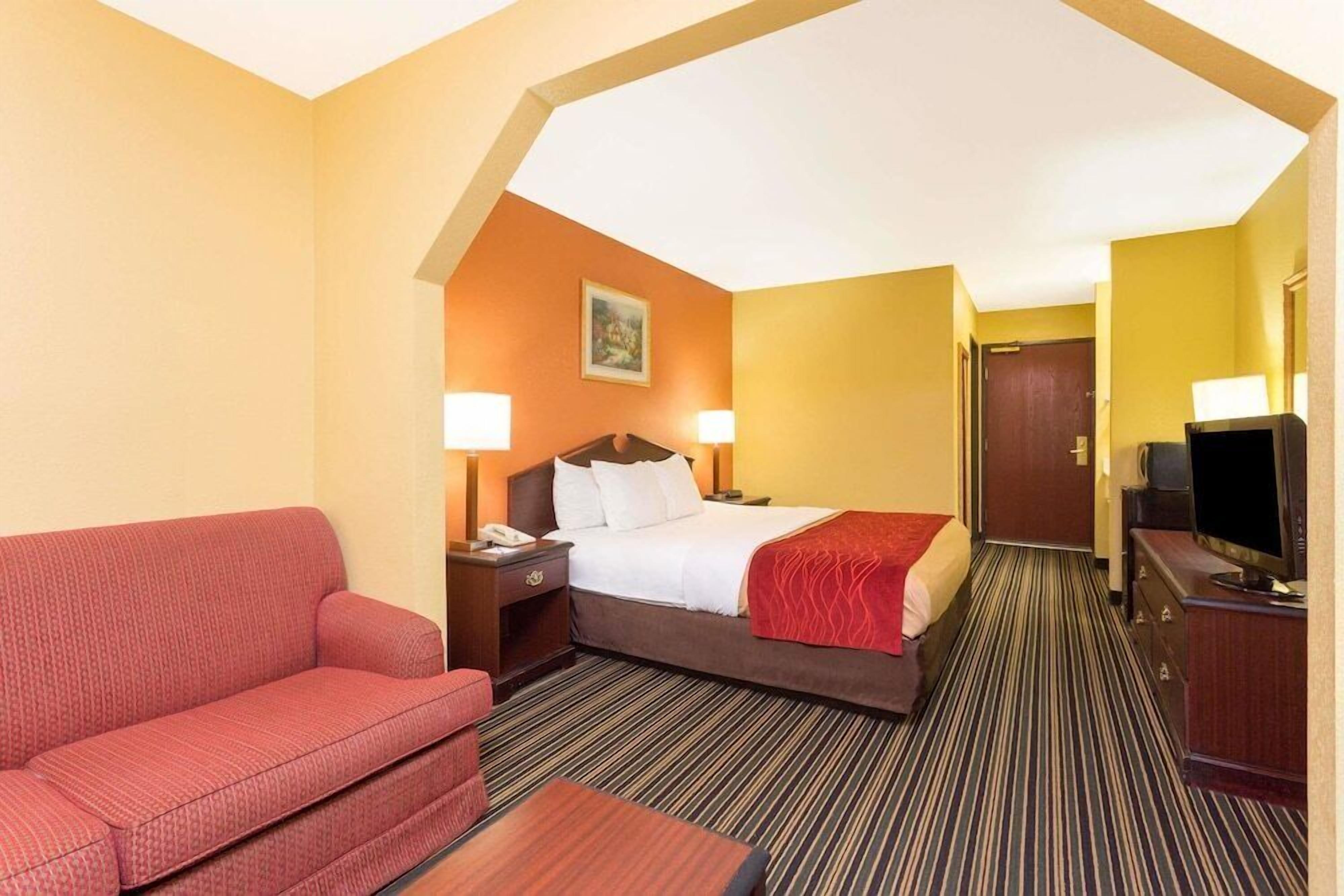 A hotel room with a bed, a red sofa, a TV, and a desk.