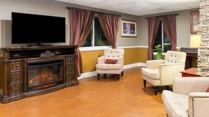 A living room with a fireplace, a television, and two armchairs. - Lux Hotel (Cordele)