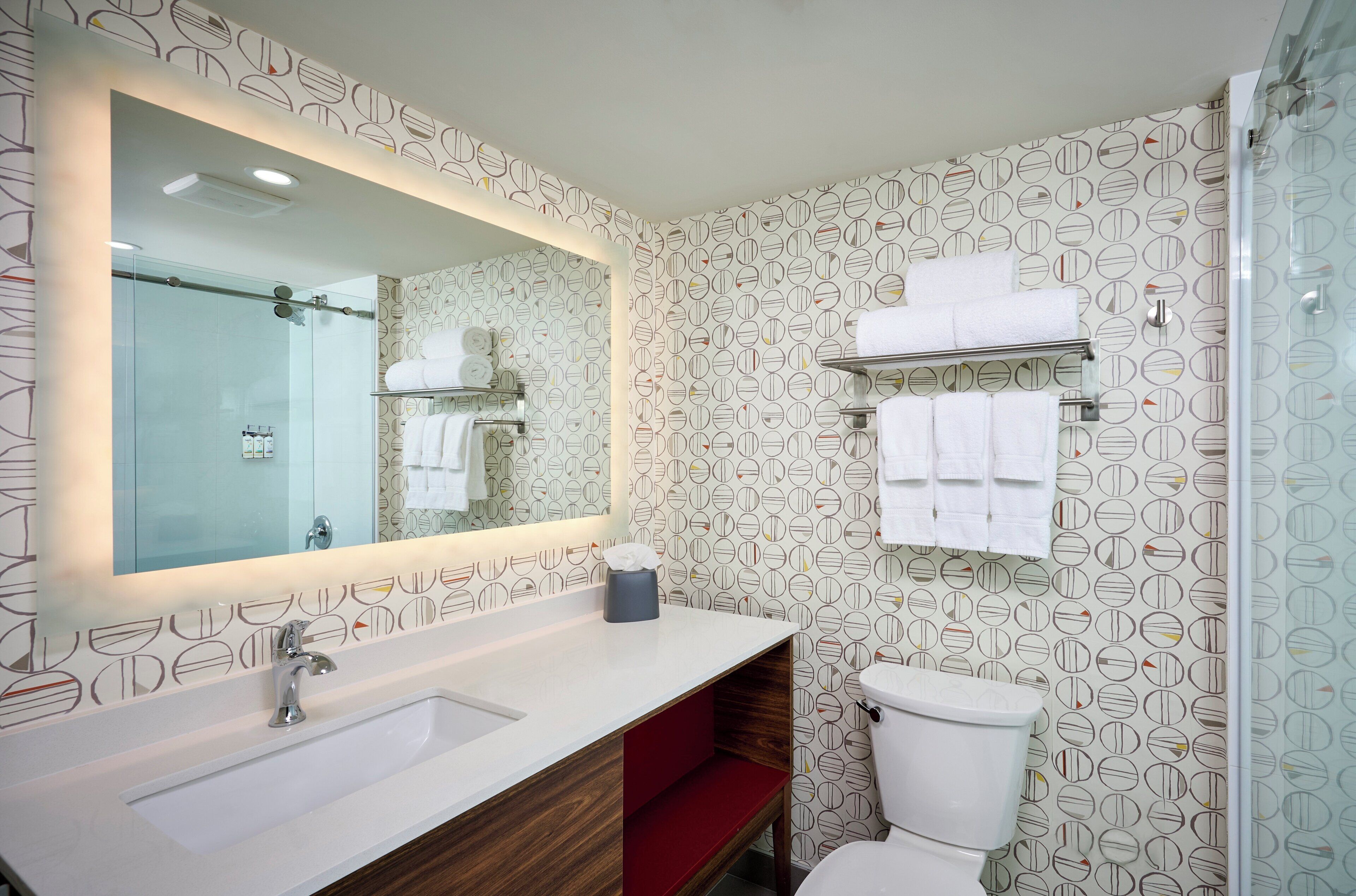 A modern bathroom with a large mirror, white sink, and a toilet.